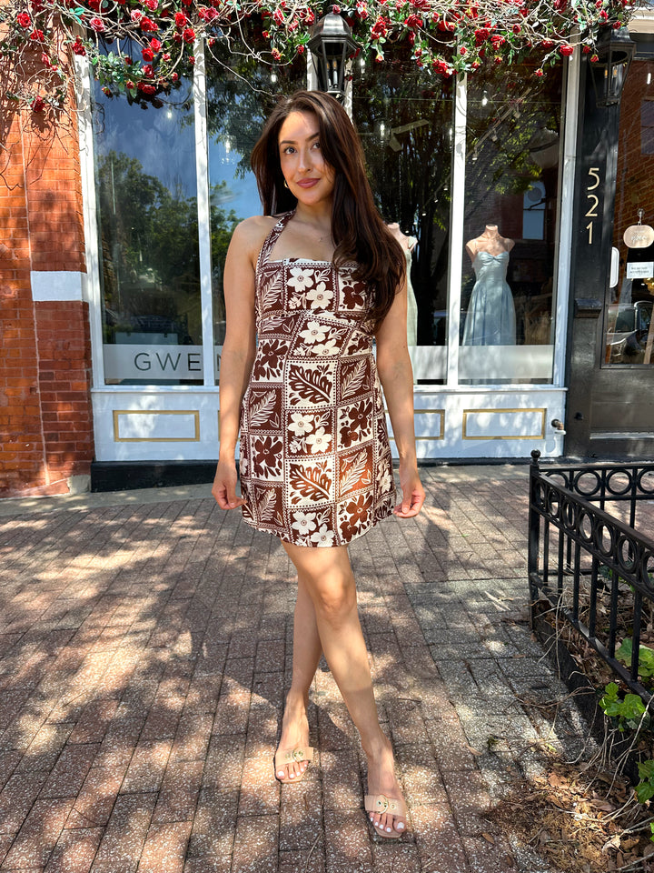 Woman wearing white and brown tropical print mini dress with square neckline.