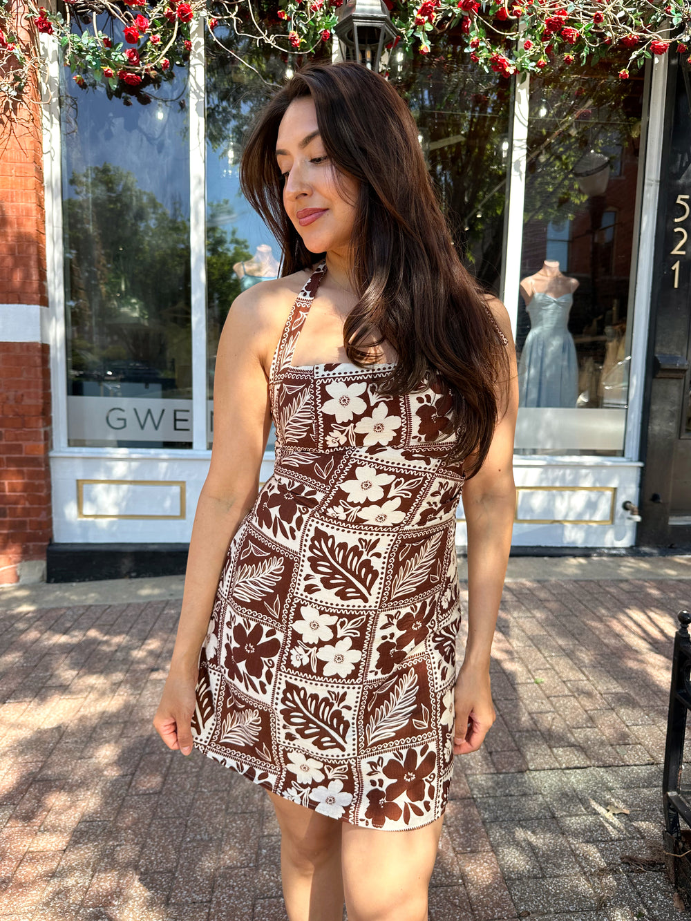 Woman wearing white and brown tropical print mini dress with square neckline.