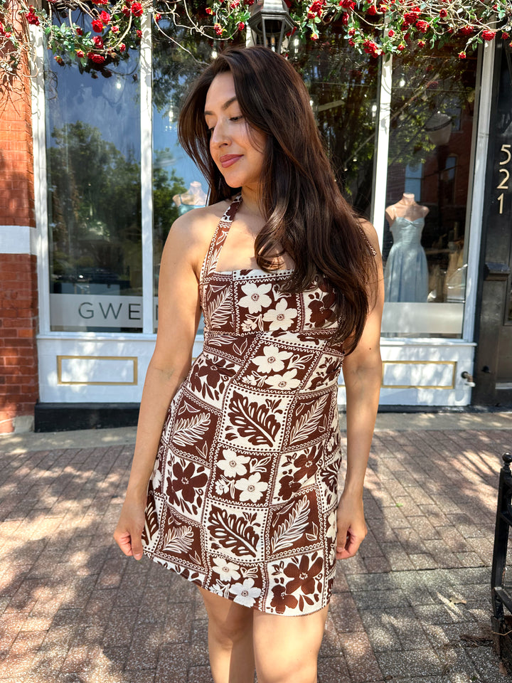 Woman wearing white and brown tropical print mini dress with square neckline.