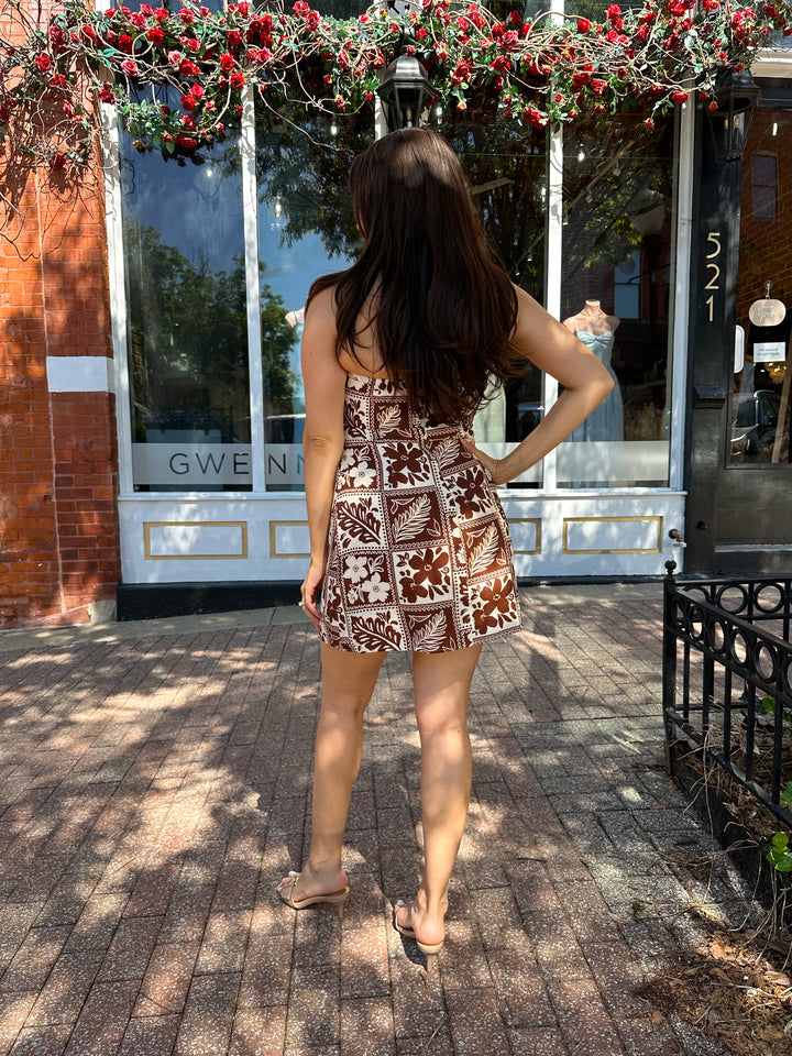 Woman wearing white and brown tropical print mini dress with square neckline.