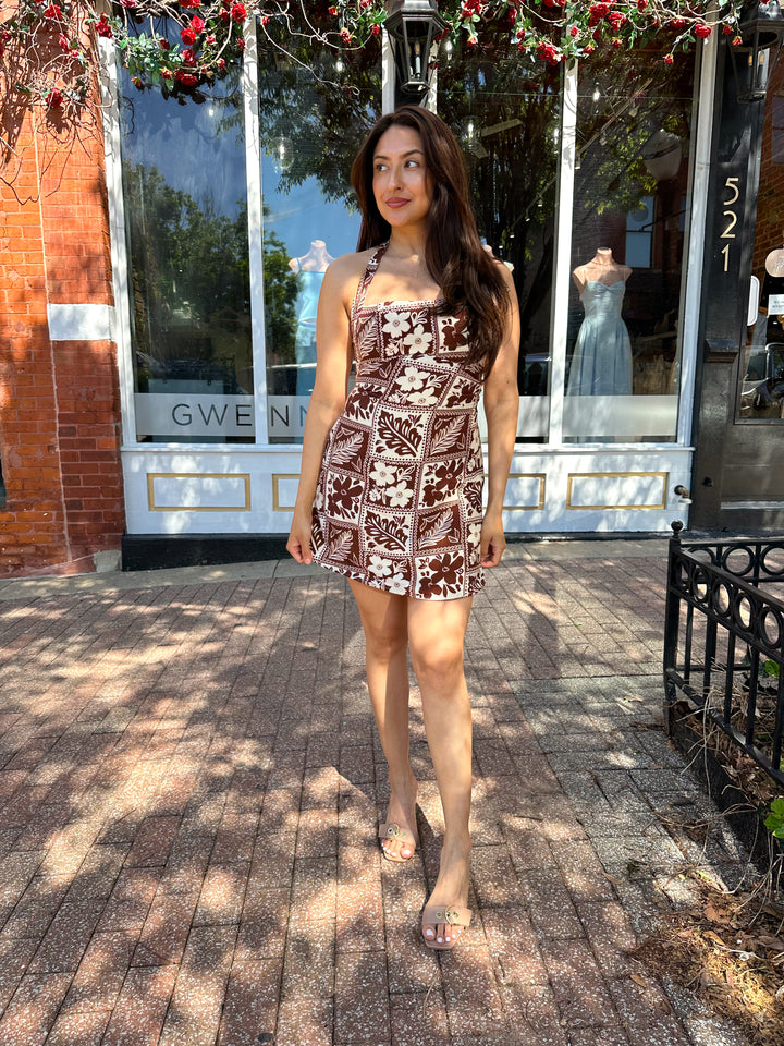 Woman wearing white and brown tropical print mini dress with square neckline.