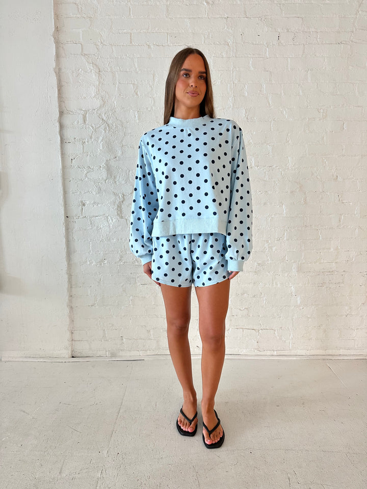 Woman wearing light blue two piece lounge set with navy polka dots. 