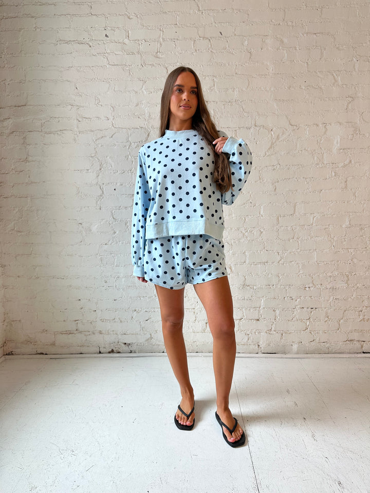 Woman wearing light blue two piece lounge set with navy polka dots. 