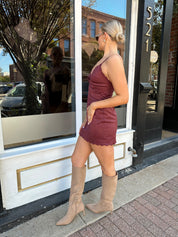 Woman wearing burgundy suede mini dress with scallop detail.
