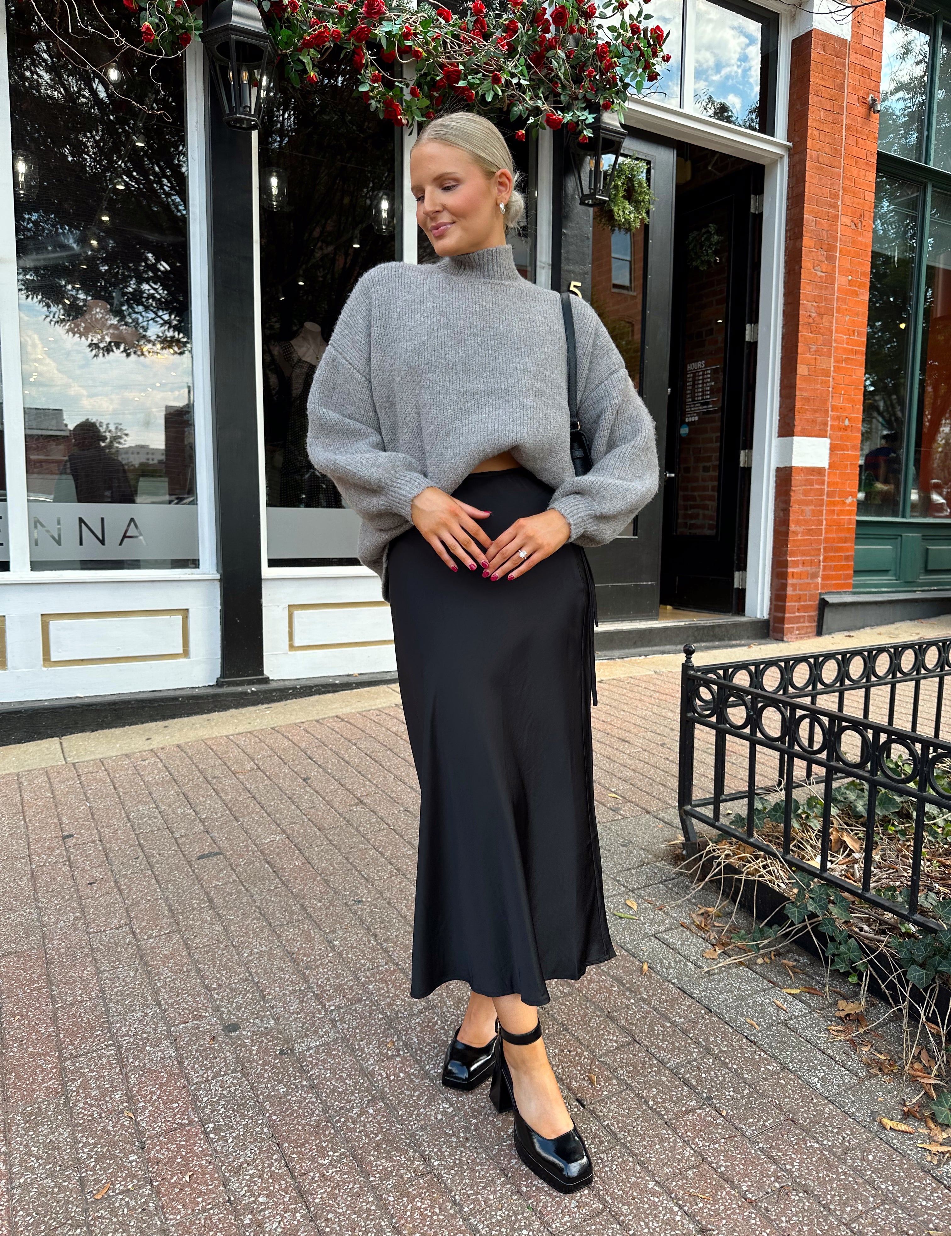 Woman wearing oversized grey turtle neck sweater with black satin skirt. 