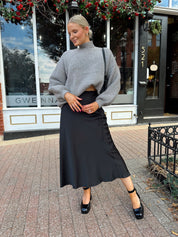 Woman wearing oversized grey turtle neck sweater with black satin skirt. 