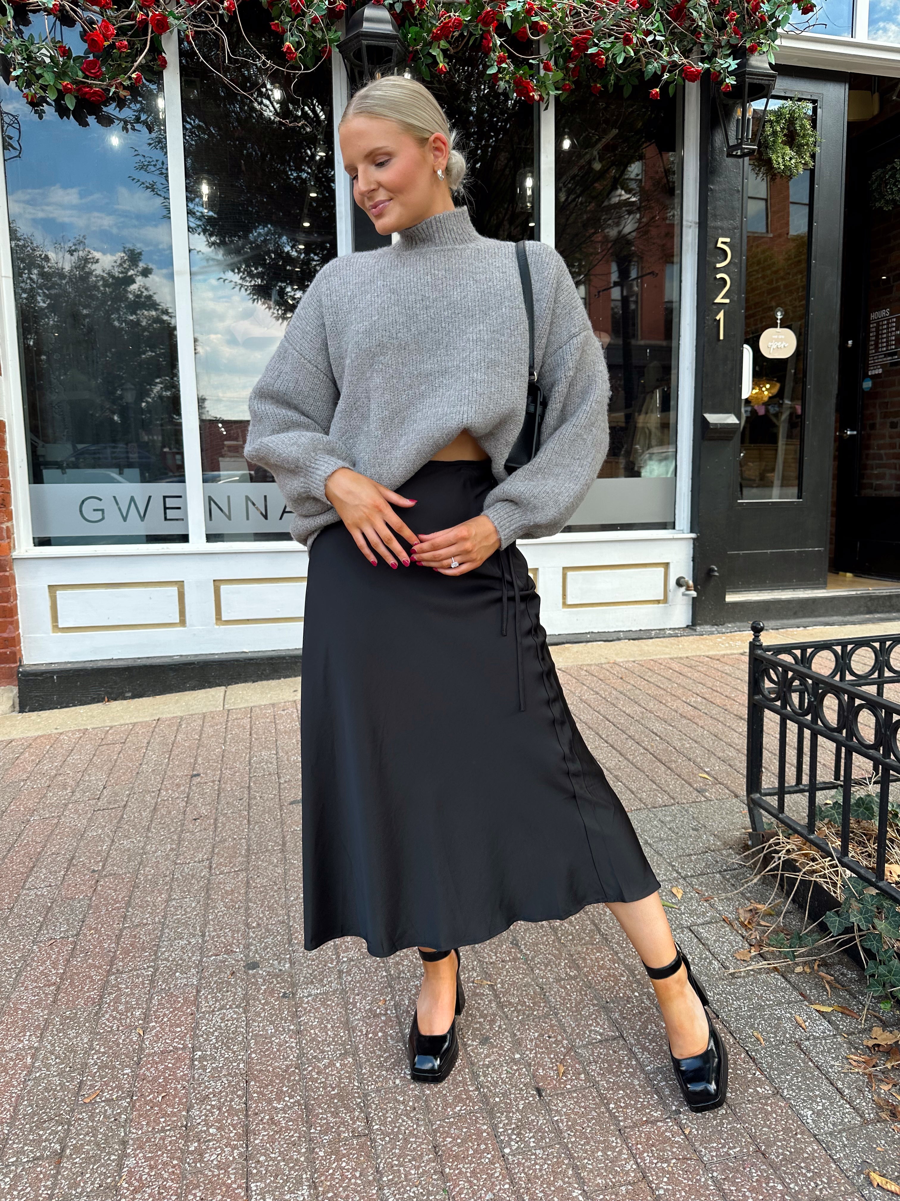 Woman wearing oversized grey turtle neck sweater with black satin skirt. 