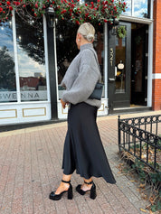 Woman wearing oversized grey turtle neck sweater with black satin skirt. 