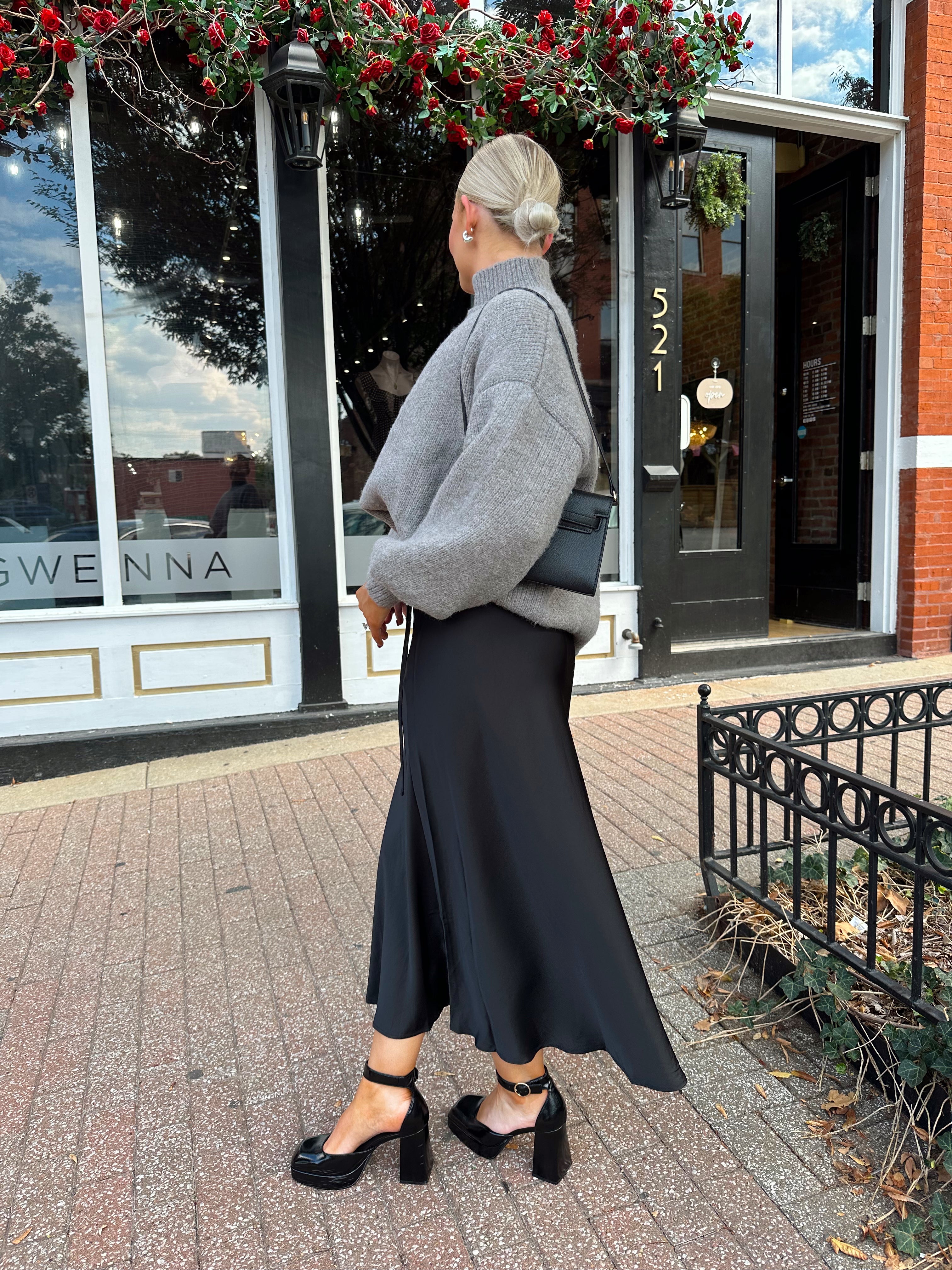Woman wearing oversized grey turtle neck sweater with black satin skirt. 