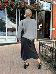 Woman wearing oversized grey turtle neck sweater with black satin skirt. 