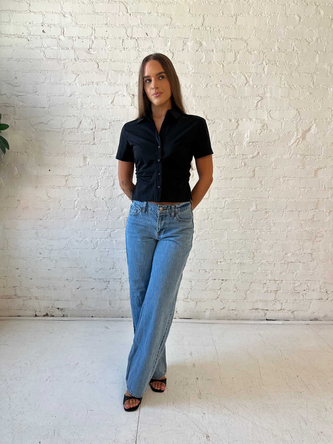 Woman wearing black short sleeve tailored button down top with medium wash jeans. 