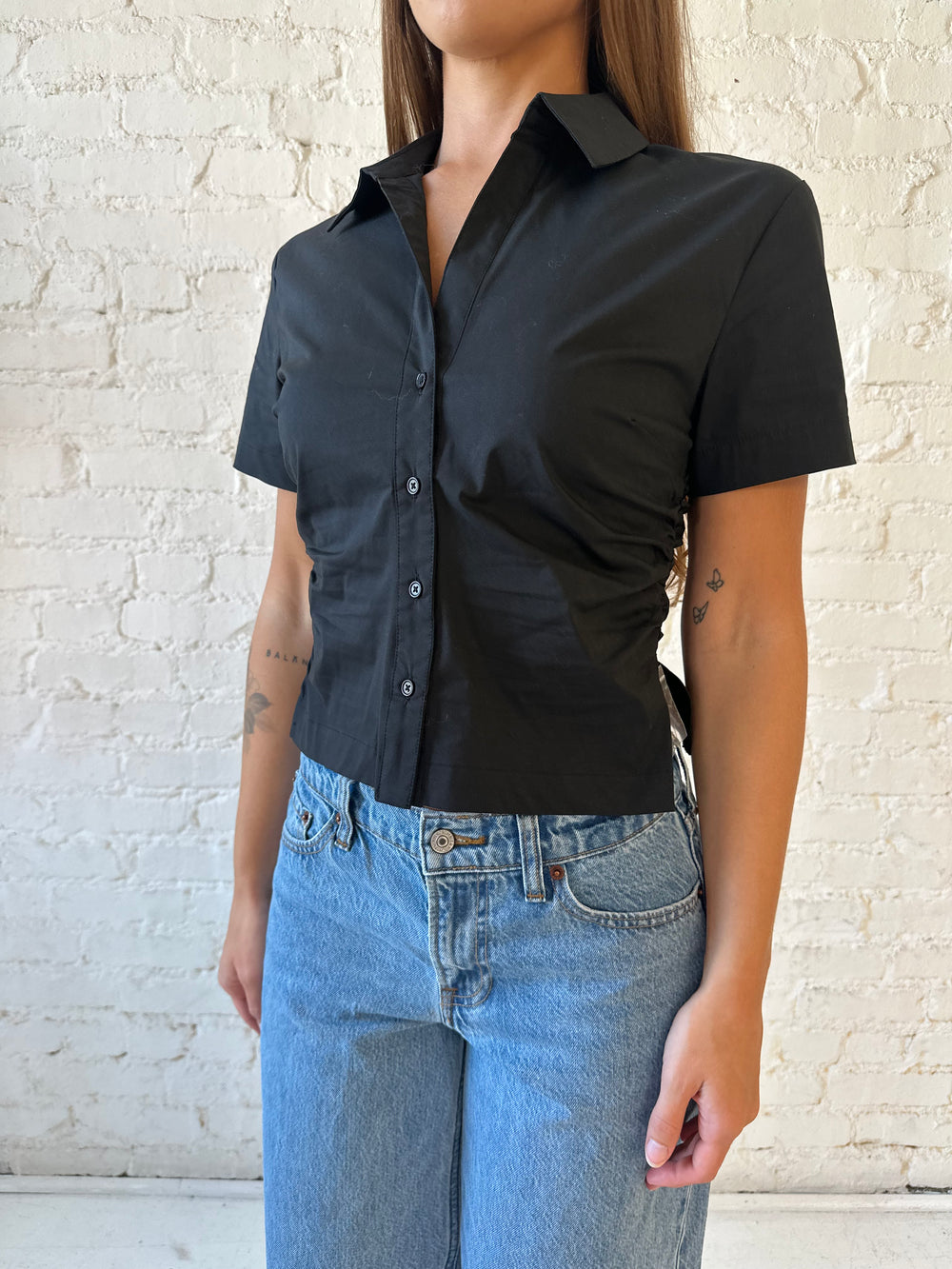Woman wearing black short sleeve tailored button down top with medium wash jeans. 