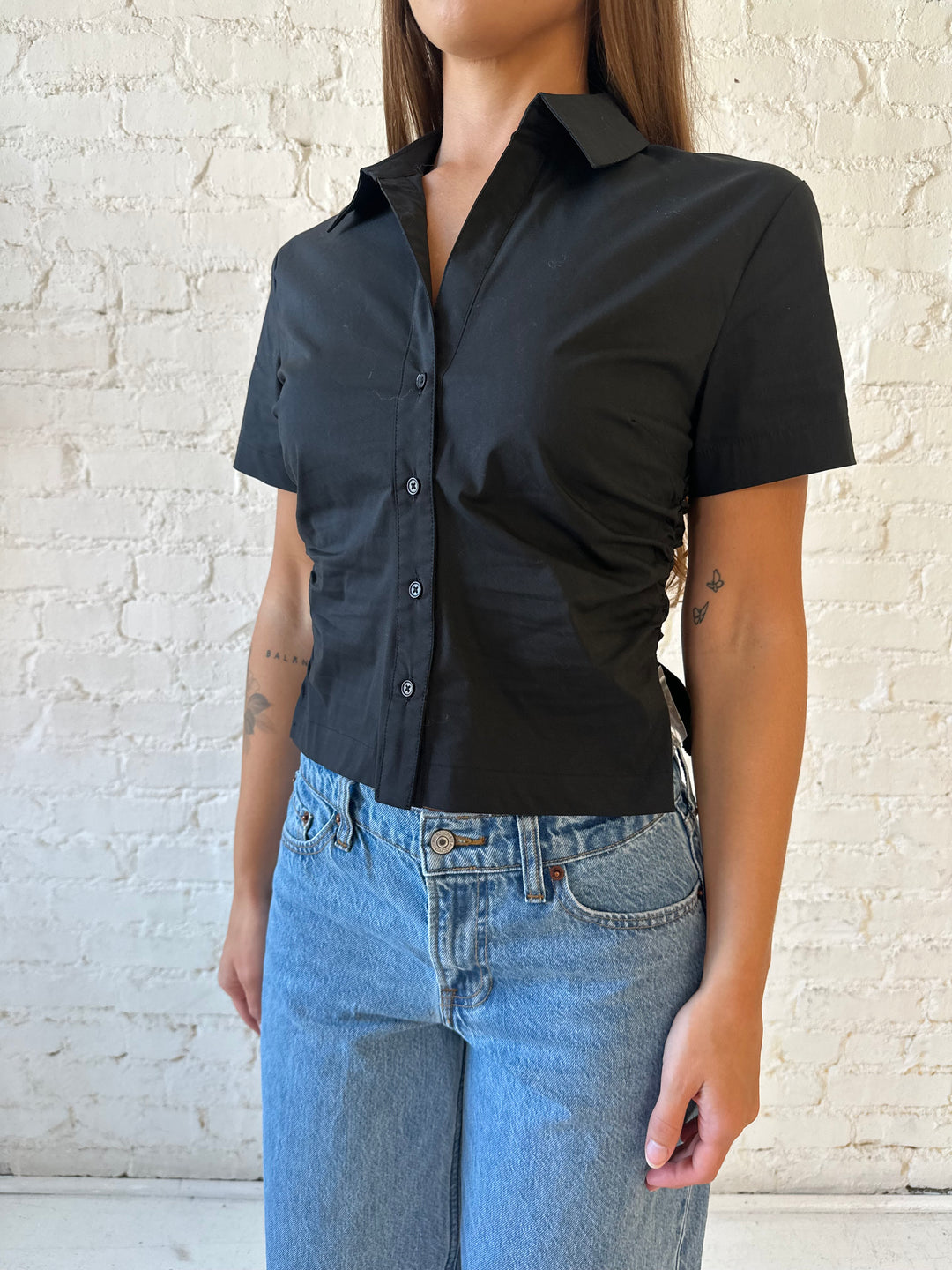 Woman wearing black short sleeve tailored button down top with medium wash jeans. 