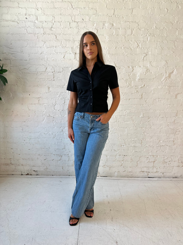 Woman wearing black short sleeve tailored button down top with medium wash jeans. 