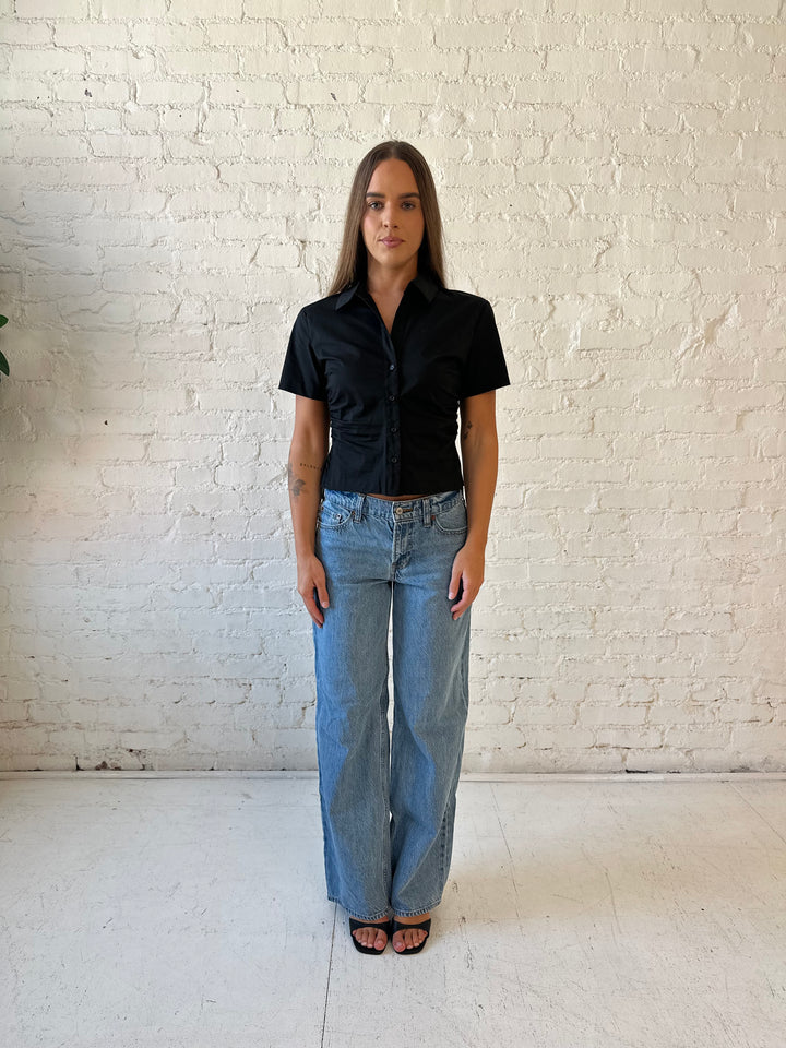 Woman wearing black short sleeve tailored button down top with medium wash jeans. 