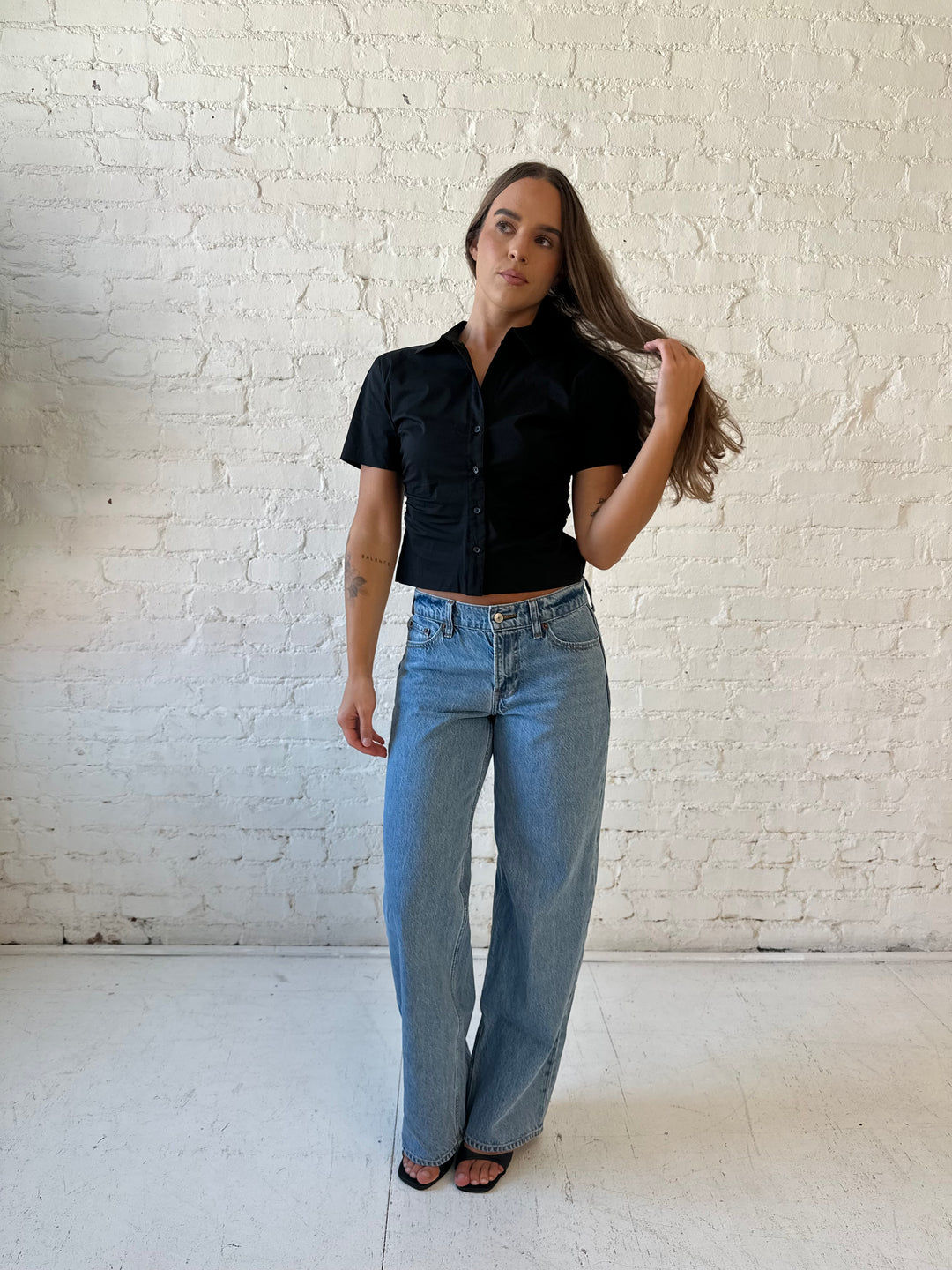 Woman wearing black short sleeve tailored button down top with medium wash jeans. 