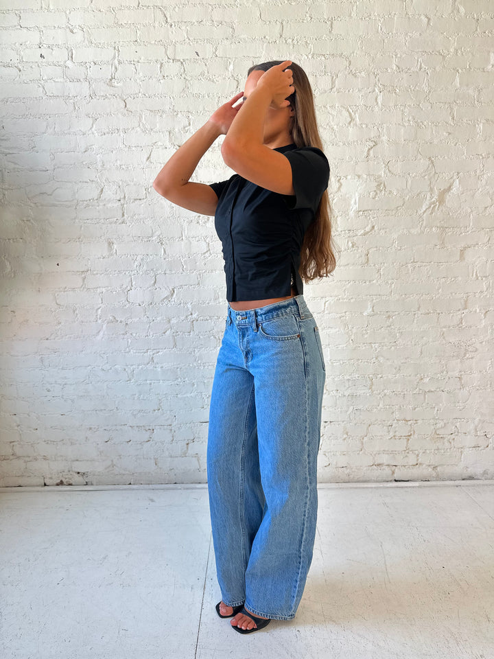 Woman wearing black short sleeve tailored button down top with medium wash jeans. 