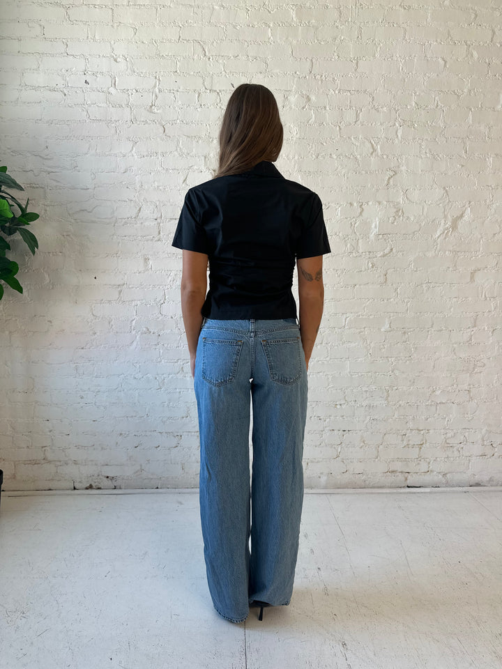 Woman wearing black short sleeve tailored button down top with medium wash jeans. 