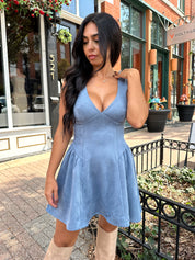 Woman wearing dusty blue suede fit to flare mini dress with v-neckline. 