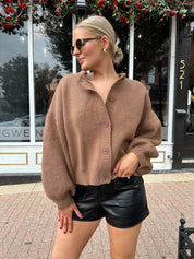 Woman wearing brown long sleeve button down cardigan with black leather shorts. 