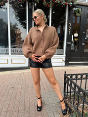 Woman wearing brown long sleeve button down cardigan with black leather shorts. 