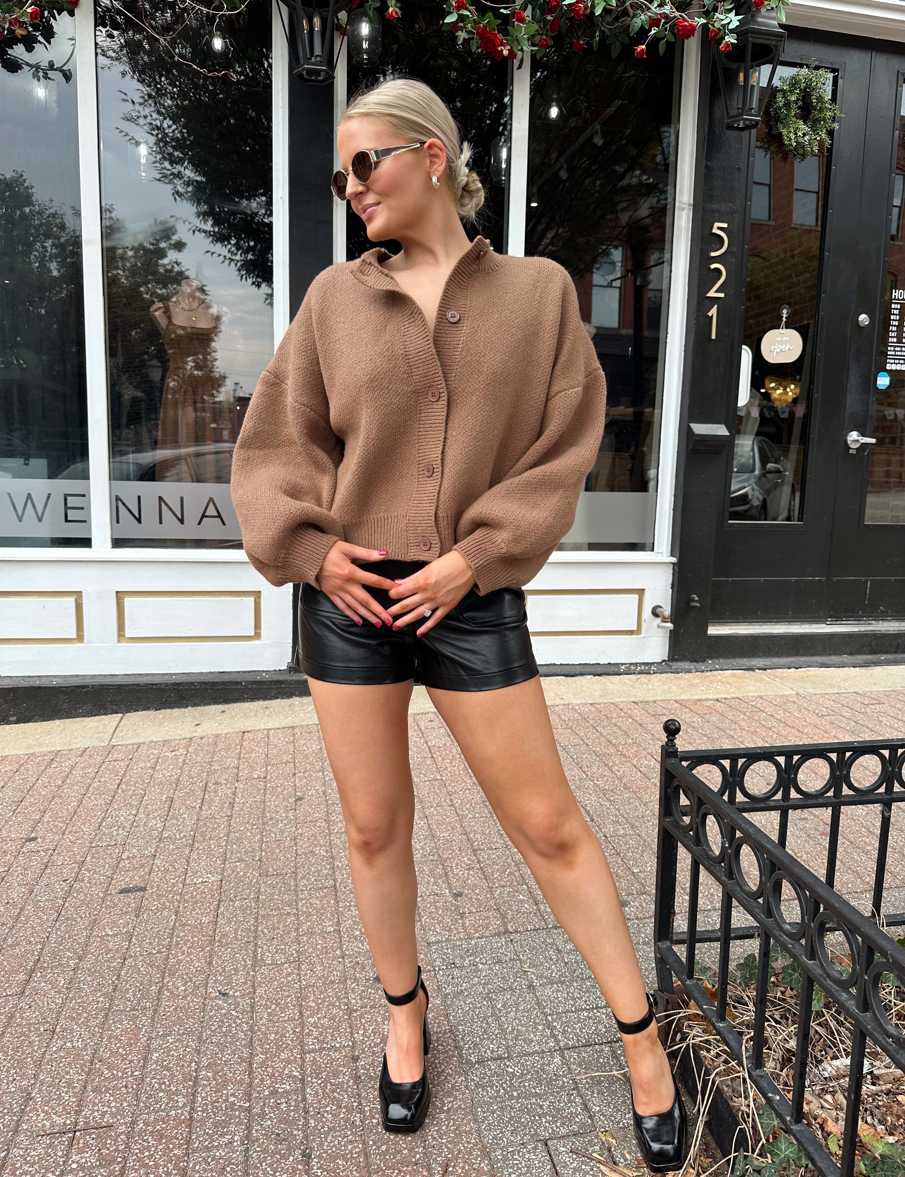 Woman wearing brown long sleeve button down cardigan with black leather shorts. 