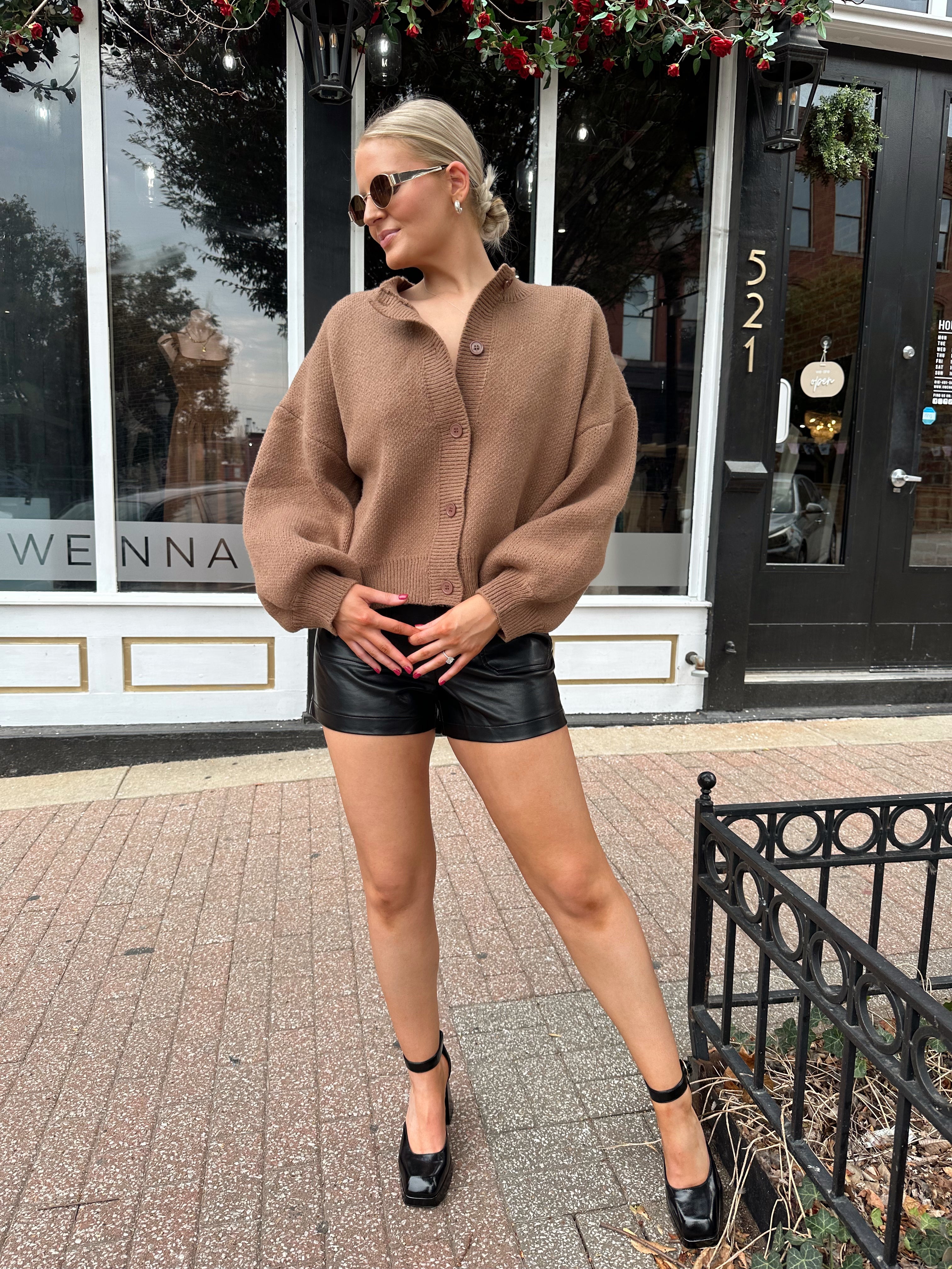 Woman wearing brown long sleeve button down cardigan with black leather shorts. 