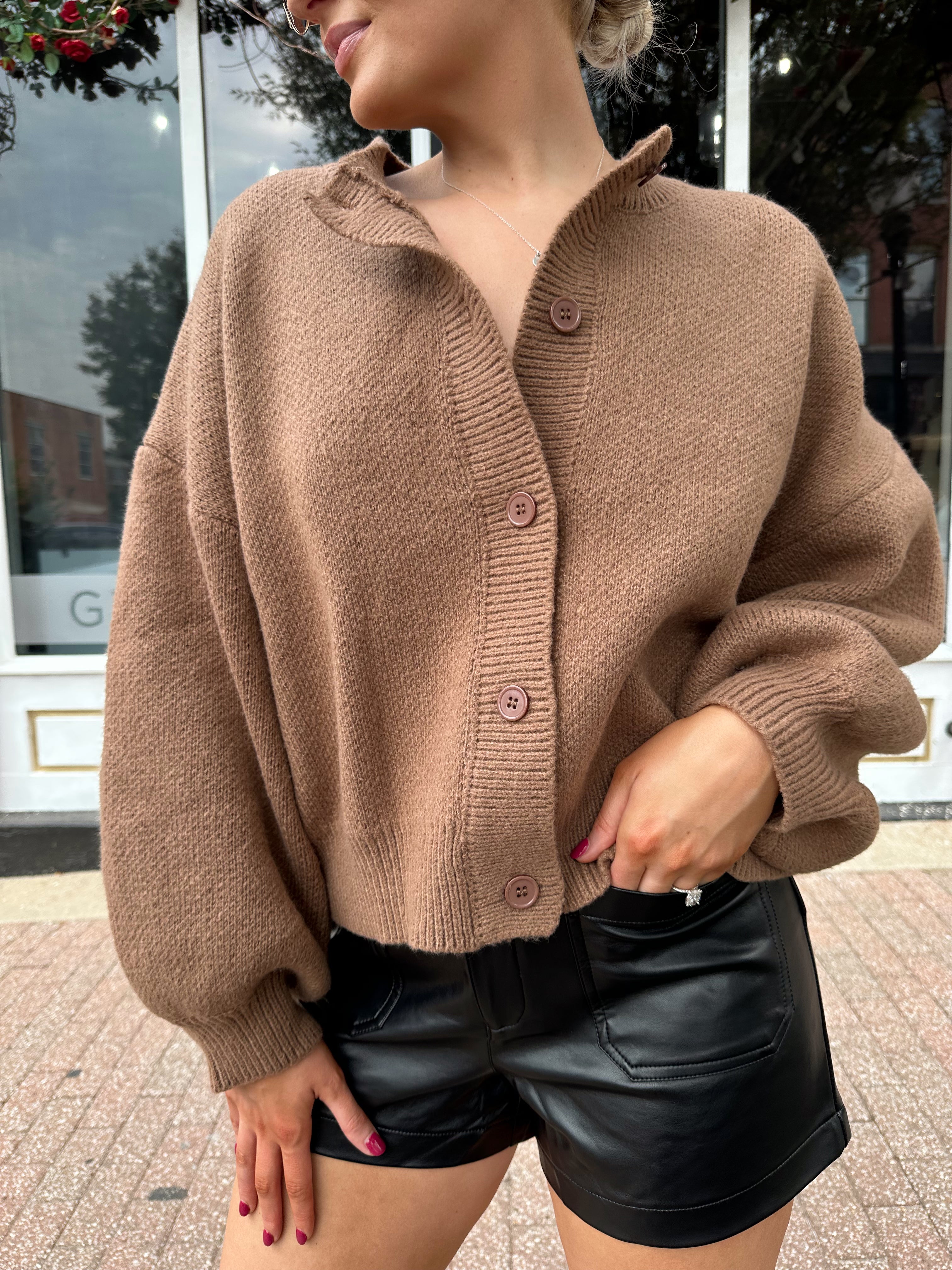 Woman wearing brown long sleeve button down cardigan with black leather shorts. 