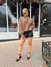 Woman wearing brown long sleeve button down cardigan with black leather shorts. 