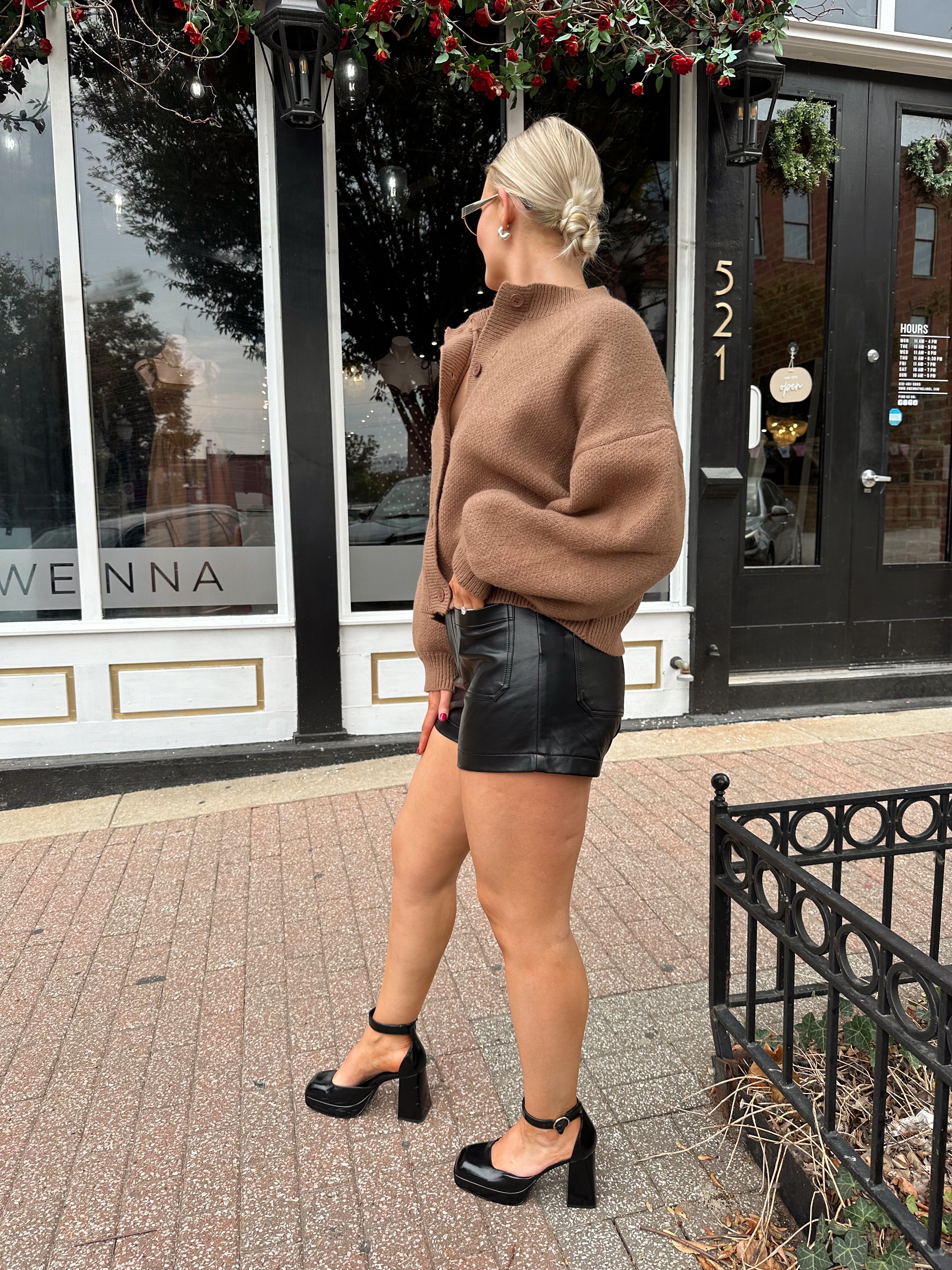 Woman wearing brown long sleeve button down cardigan with black leather shorts. 