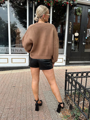 Woman wearing brown long sleeve button down cardigan with black leather shorts. 