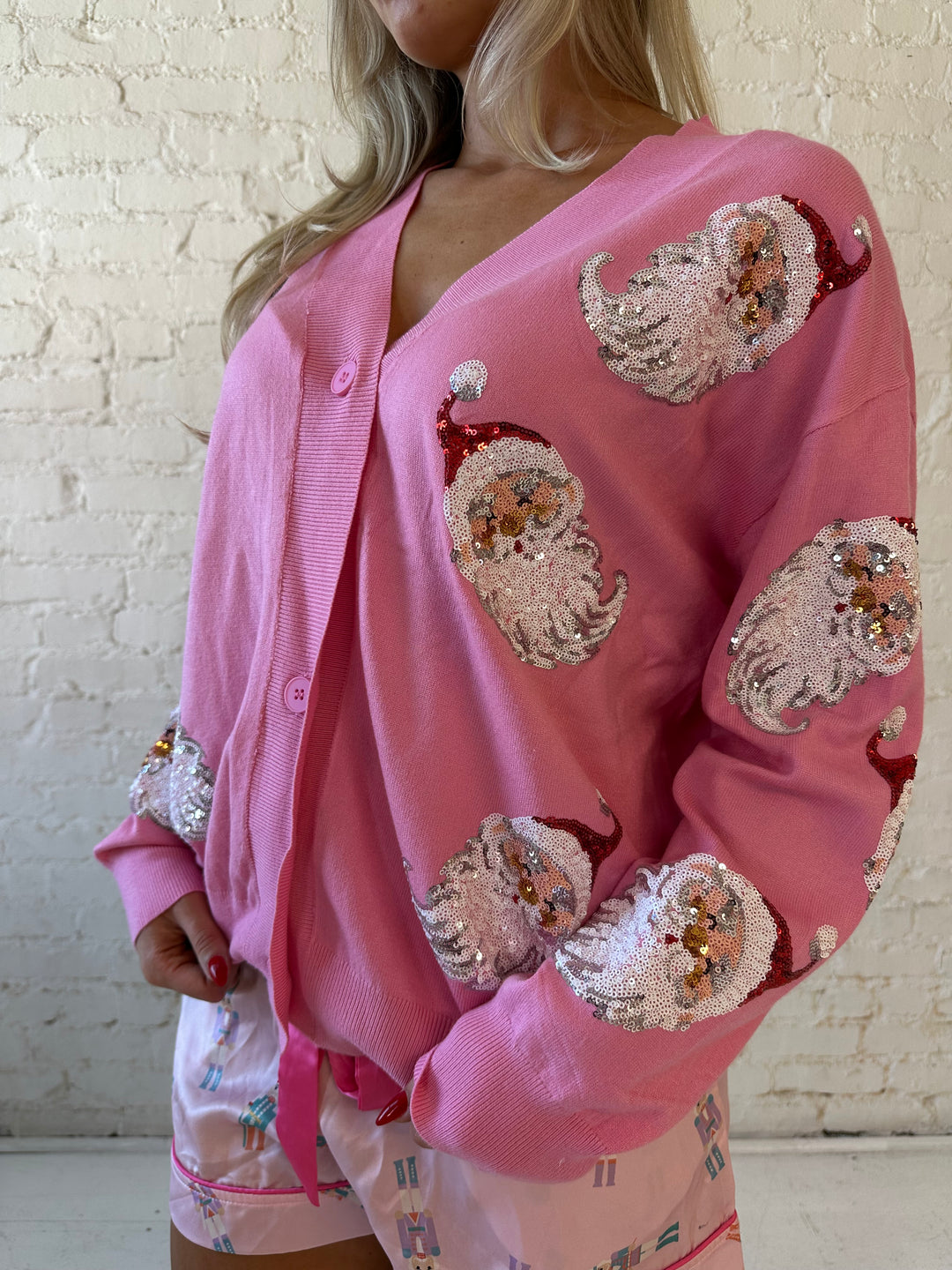 Woman wearing bubble gum pink knit cardigan with sequin santas all over.