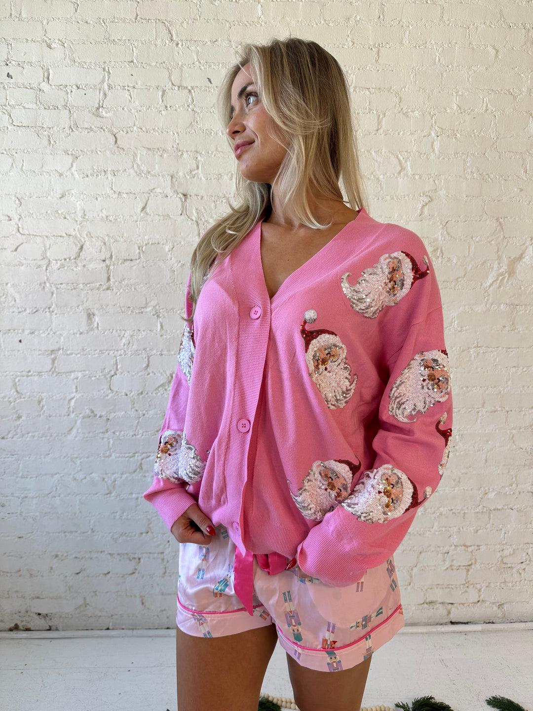Woman wearing bubble gum pink knit cardigan with sequin santas all over.