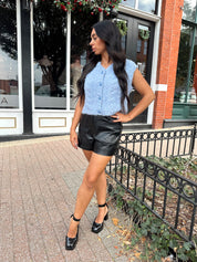 Woman wearing light blue knit sleeveless sweater vest with rose button detailing closure. 
