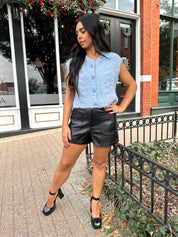 Woman wearing light blue knit sleeveless sweater vest with rose button detailing closure. 