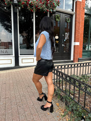 Woman wearing light blue knit sleeveless sweater vest with rose button detailing closure. 