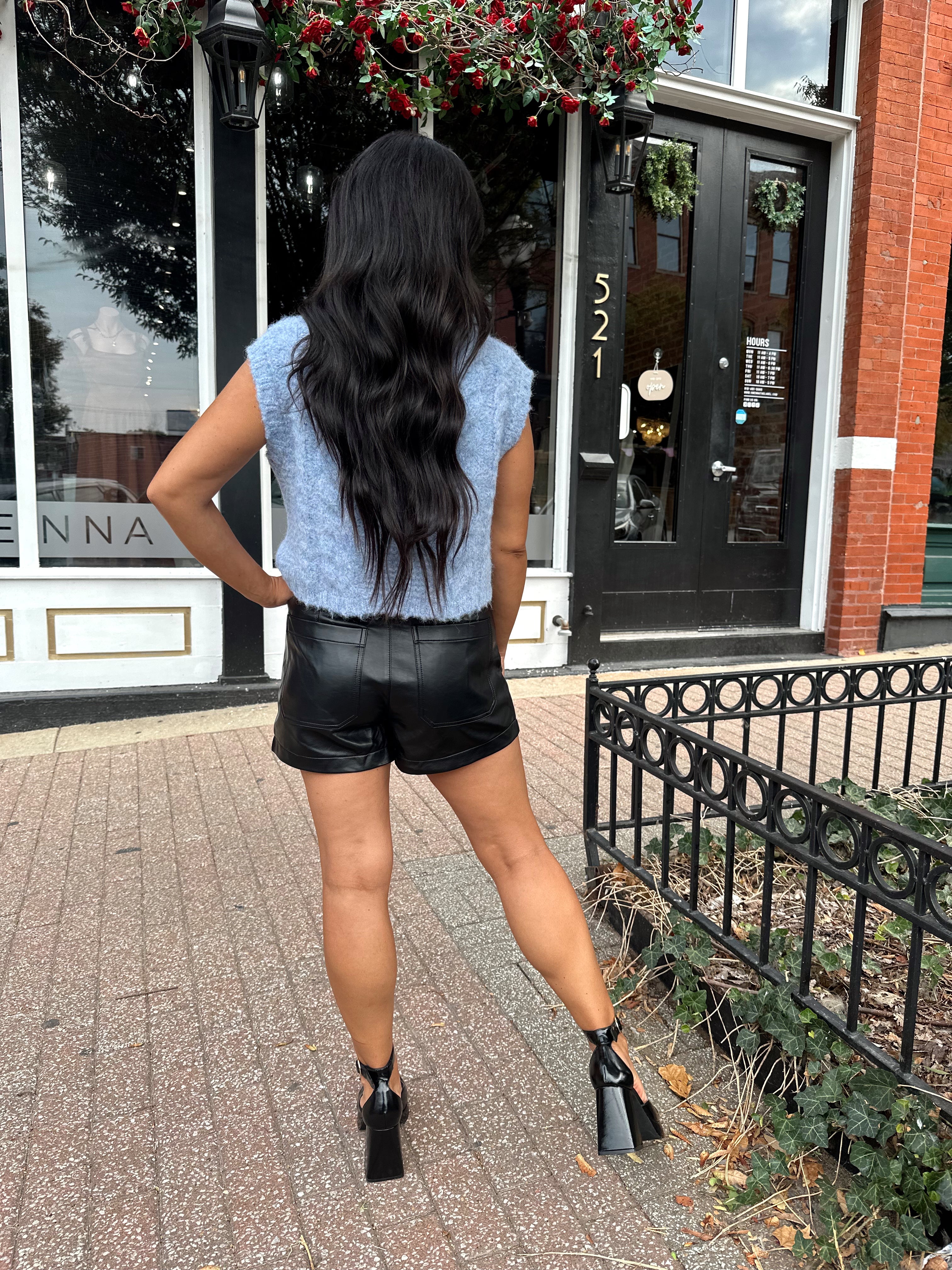 Woman wearing light blue knit sleeveless sweater vest with rose button detailing closure. 