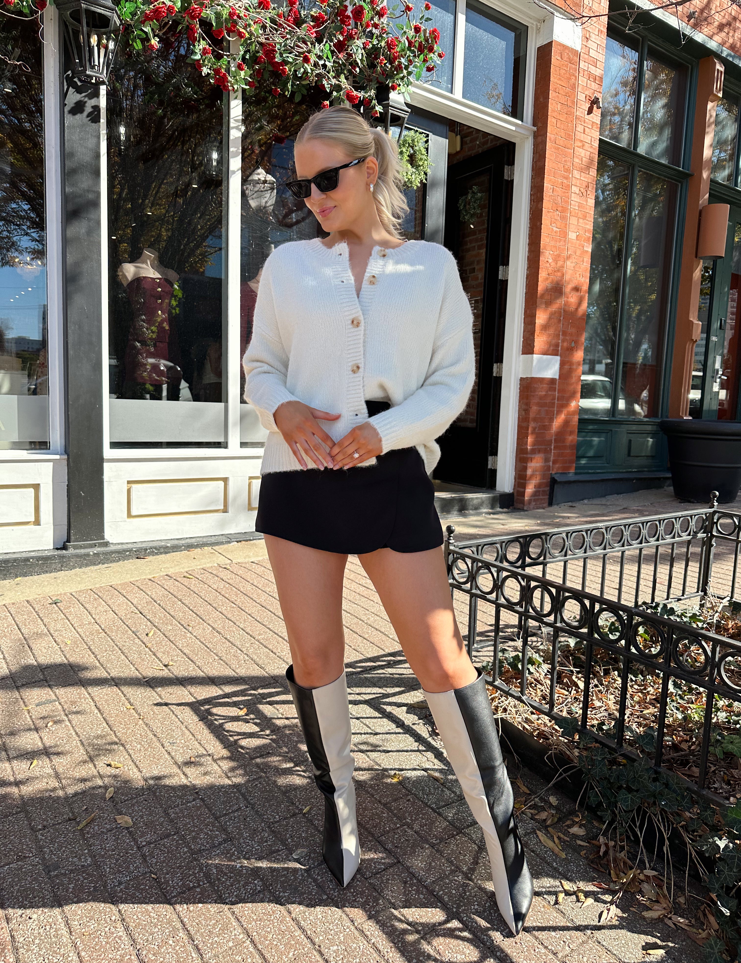 Woman wearing cream knit button down cardigan with black mini skirt. 
