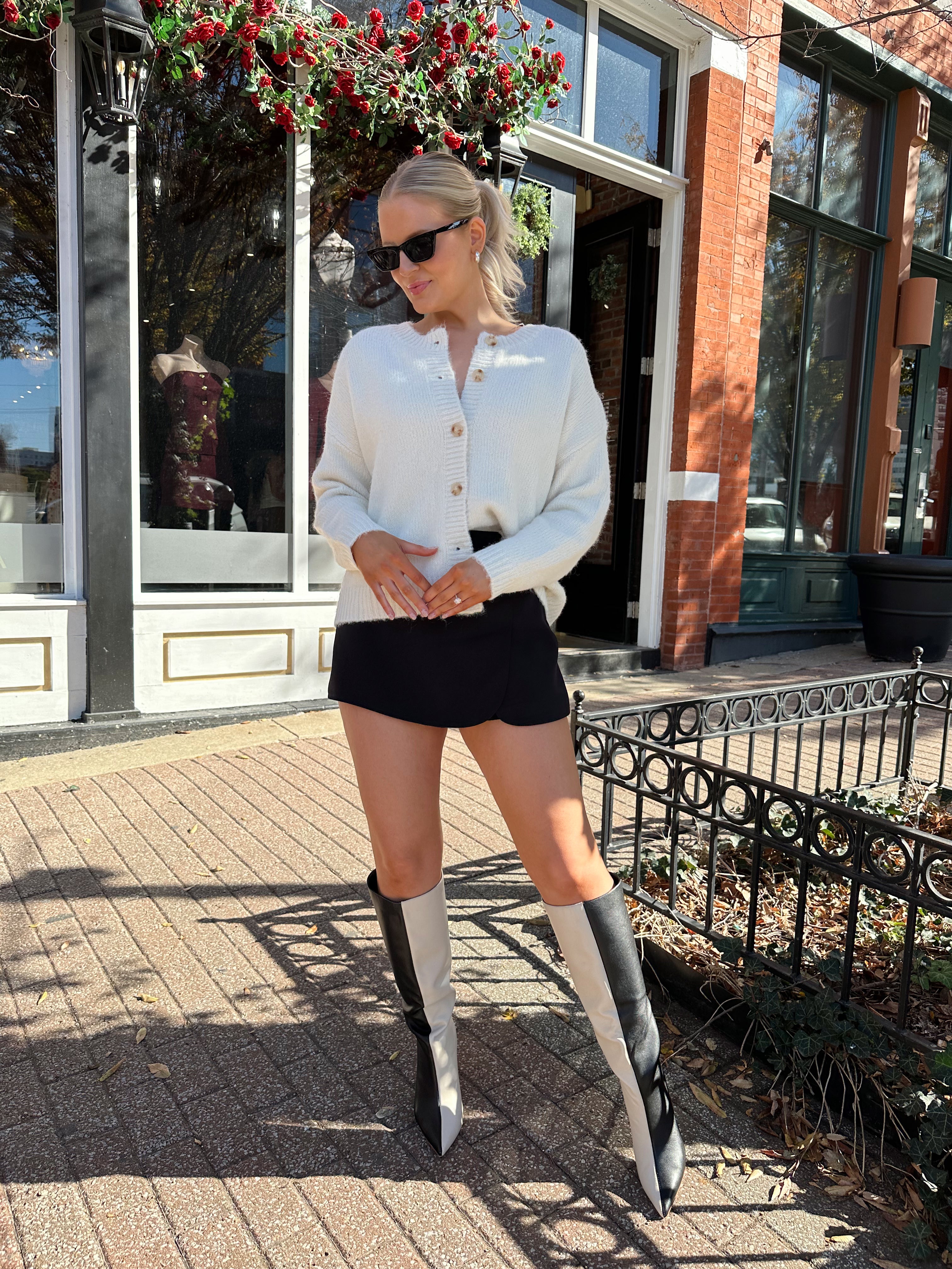 Woman wearing cream knit button down cardigan with black mini skirt. 