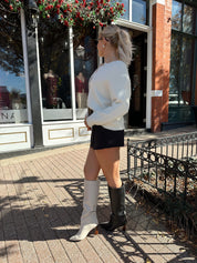 Woman wearing cream knit button down cardigan with black mini skirt. 