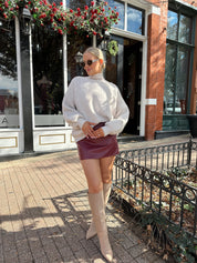 Woman wearing burgundy leather mini dress with stone knit turtle neck sweater.
