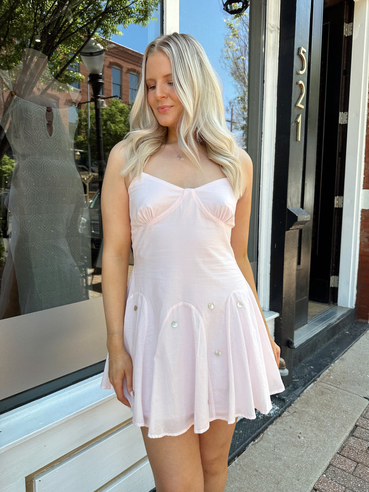 Woman wearing linen pink mini dress with a fit to flare style, and iridescent beading. 