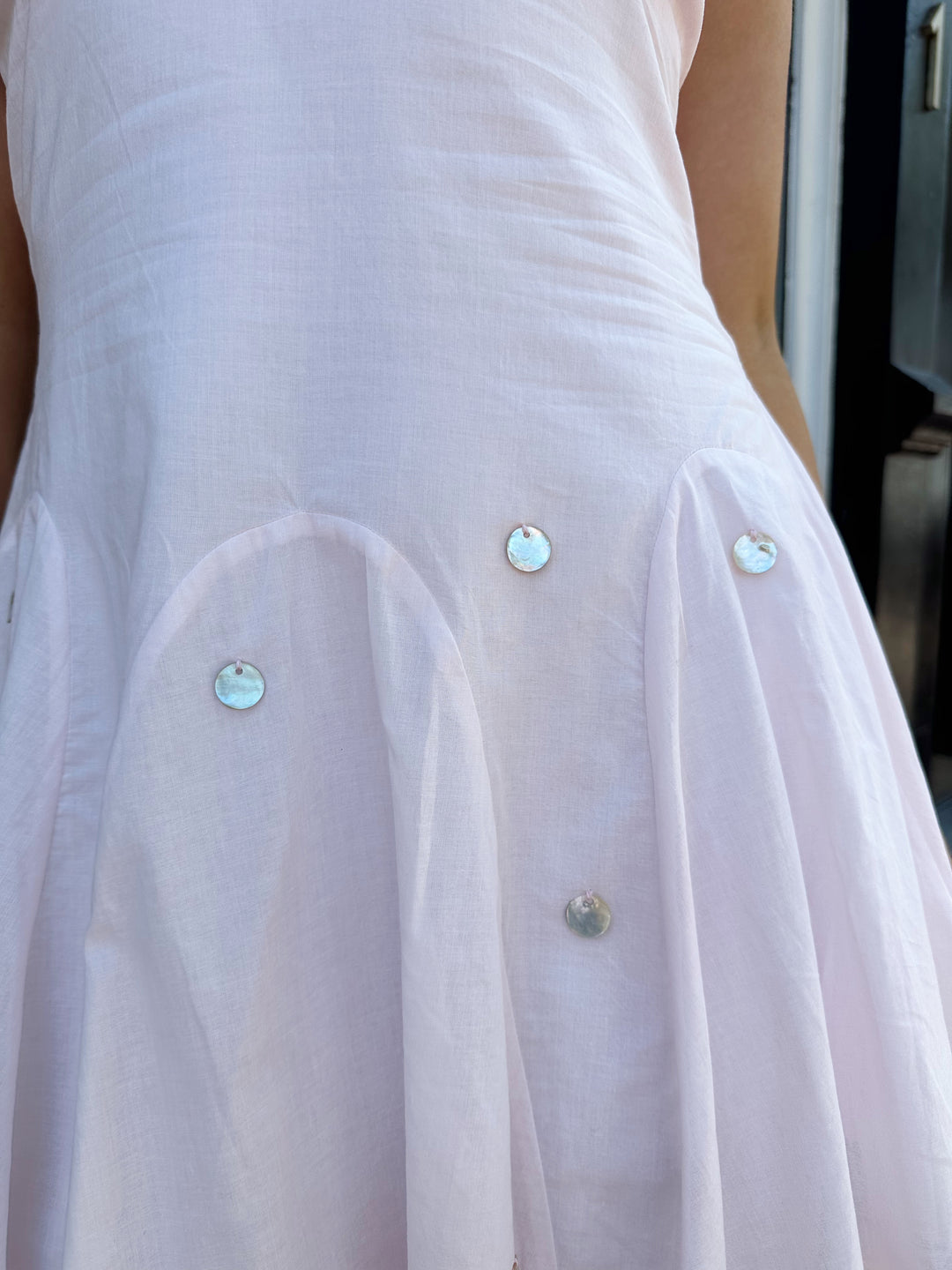 Woman wearing linen pink mini dress with a fit to flare style, and iridescent beading. 