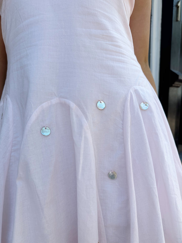 Woman wearing linen pink mini dress with a fit to flare style, and iridescent beading. 