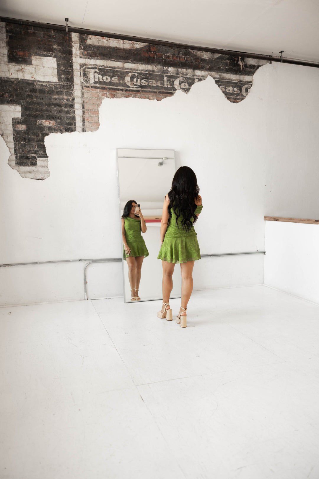 Woman wearing an olive green jacquard mini dress with off the shoulder neckline. 