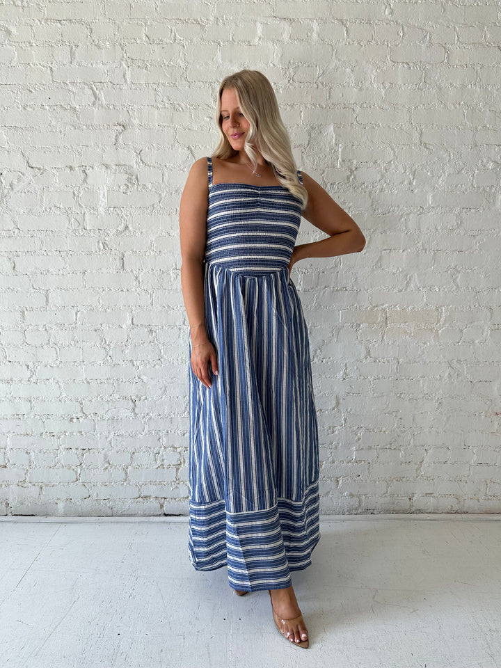 Woman wearing blue striped maxi dress with a smocked bodice, and adjustable straps. 