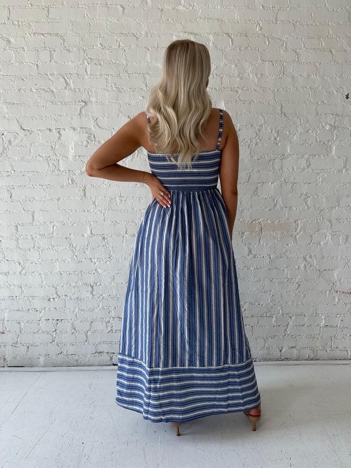Woman wearing blue striped maxi dress with a smocked bodice, and adjustable straps. 