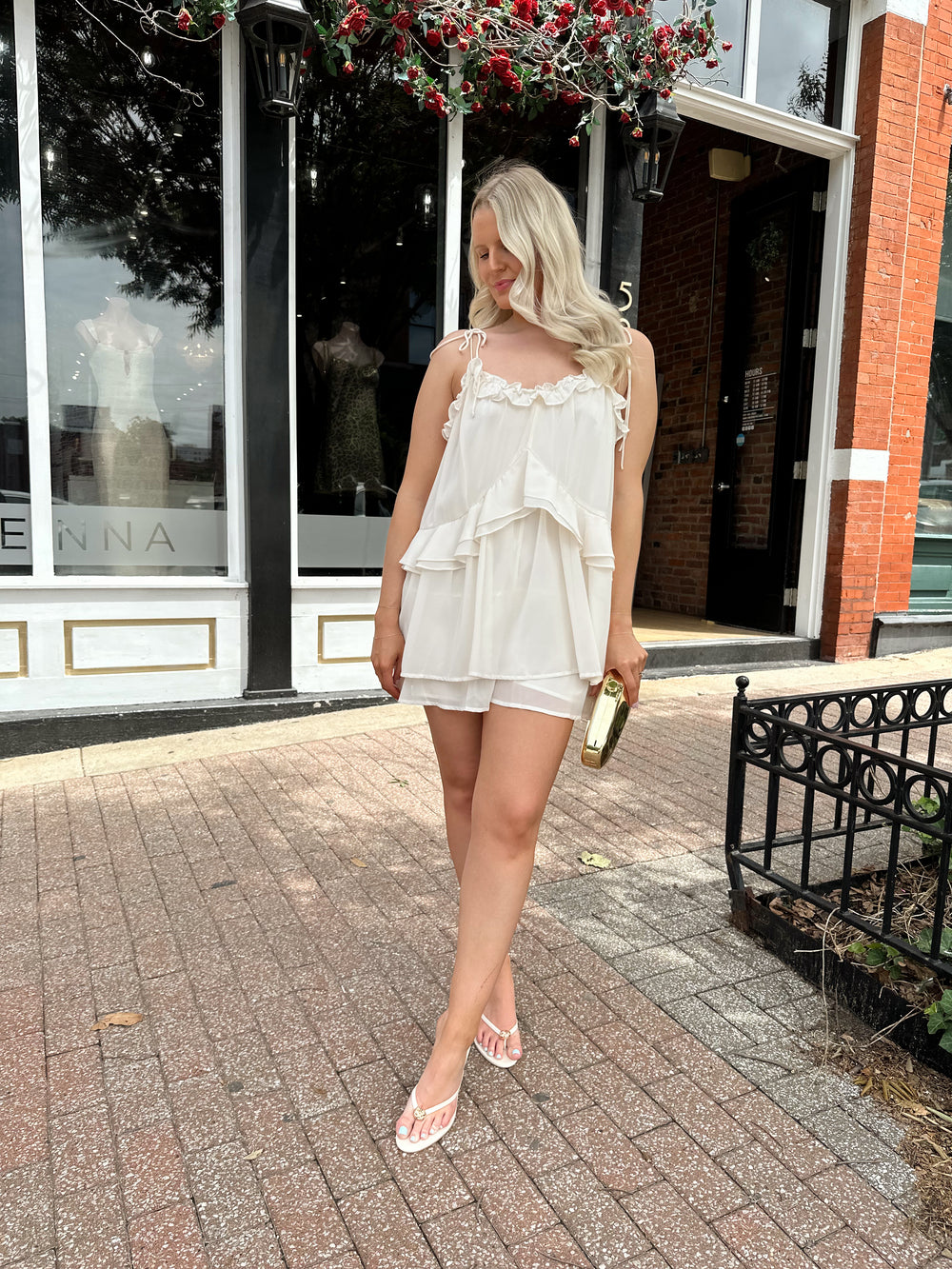 Woman wearing ivory colored romper with ruffle tiered detailing, and self tie straps.