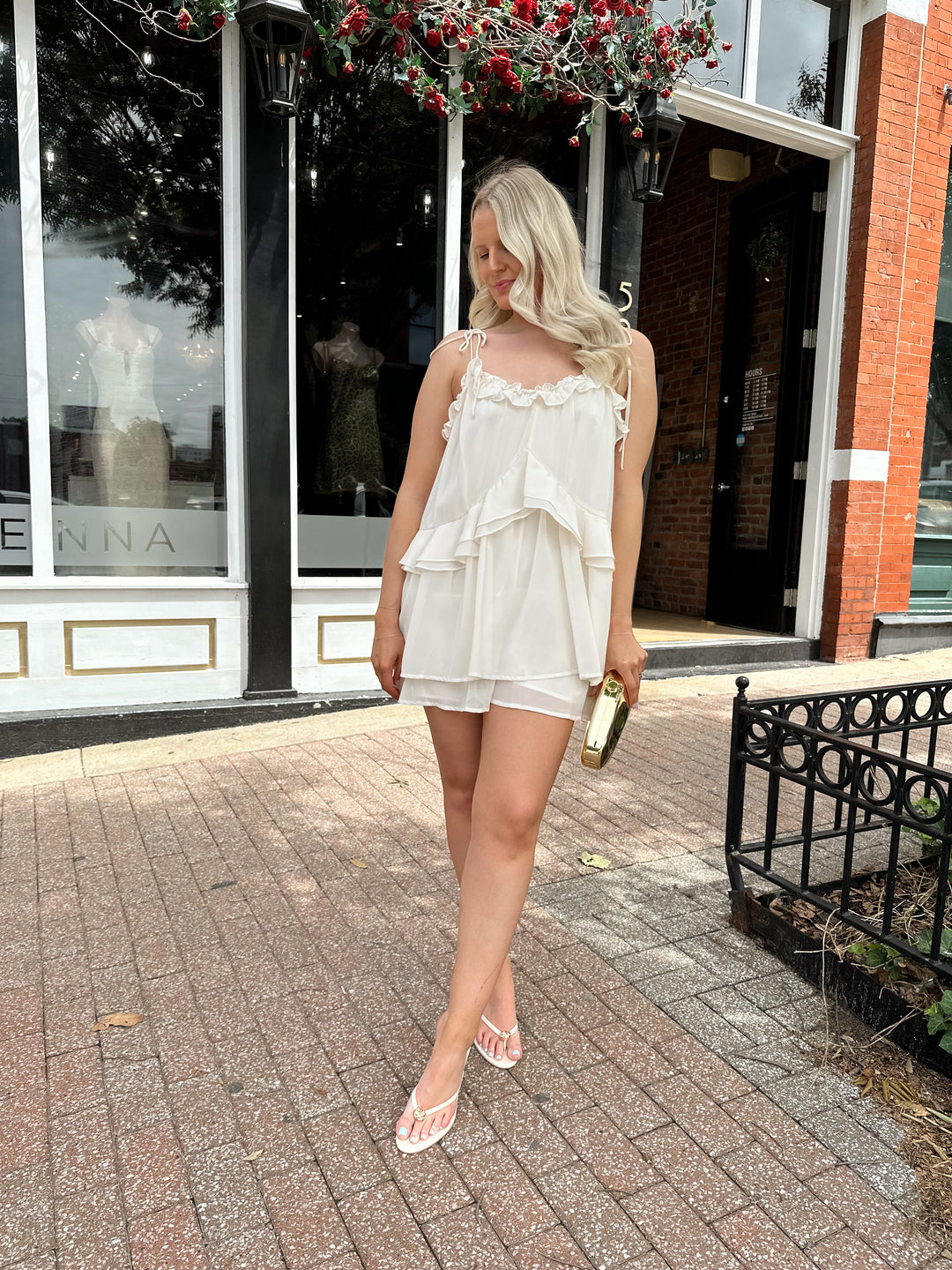 Woman wearing ivory colored romper with ruffle tiered detailing, and self tie straps.