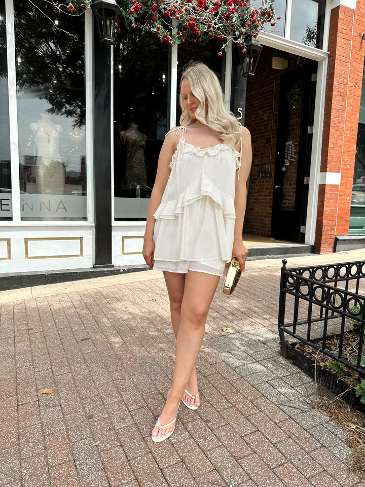 Woman wearing ivory colored romper with ruffle tiered detailing, and self tie straps.